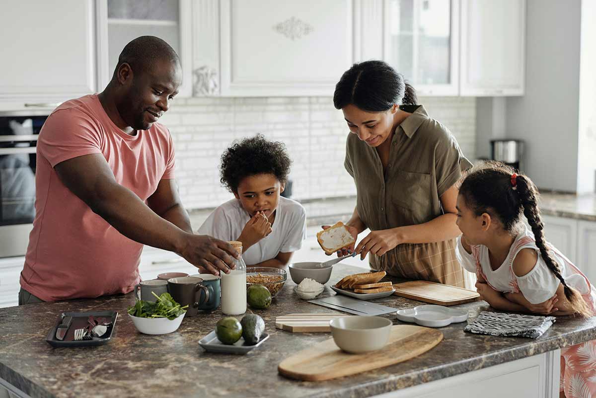 A happy family of four prepares food in the kitchen. 